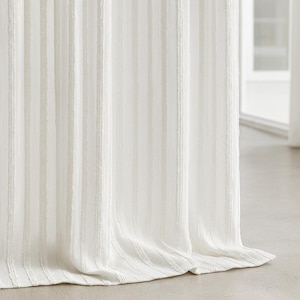 Puede incluir: Cortina texturizada blanquecina con rayas verticales. La tela se pliega suavemente, creando una sensación de profundidad y textura. La cortina está hecha de un material claro, adecuado para la decoración del hogar.