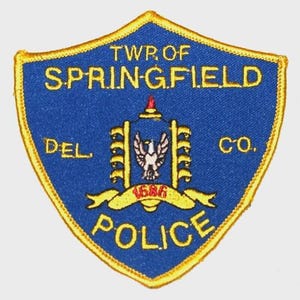 May include: A blue and gold police patch with the words "TWP. OF SPRINGFIELD" and "DEL. CO." The patch features a central emblem with a bird and the word "POLICE".