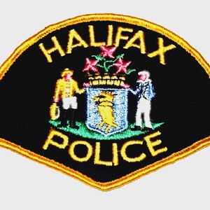 May include: Embroidered Halifax Police patch with a black background and gold trim. The patch features the words "HALIFAX POLICE" in gold, and a central emblem with figures and a crest.