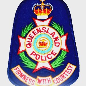 May include: A blue patch featuring the Queensland Police emblem. The emblem includes a crown, a cross, and the words "QUEENSLAND POLICE" in a circular design. The words "FIRMNESS WITH COURTESY" are displayed below.