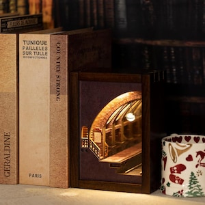 May include: A wooden book nook with a detailed, illuminated interior scene of a brick archway and stairs. The book nook is nestled among several books, including one with the title "Country Strong."