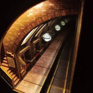 May include: A miniature diorama of a vintage subway station, featuring brick archways, tiled platforms, and the sign "BAKER STREET". Overhead, spherical lights illuminate the scene. The overall color palette is warm, with browns and golds.