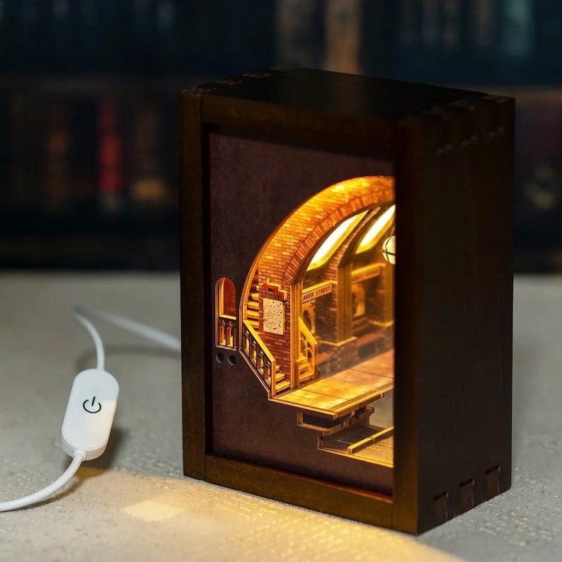 May include: A wooden, illuminated book nook featuring a detailed, layered design of a brick archway and staircase. The interior scene is lit with warm light, and the exterior is a dark brown box with a white power switch.