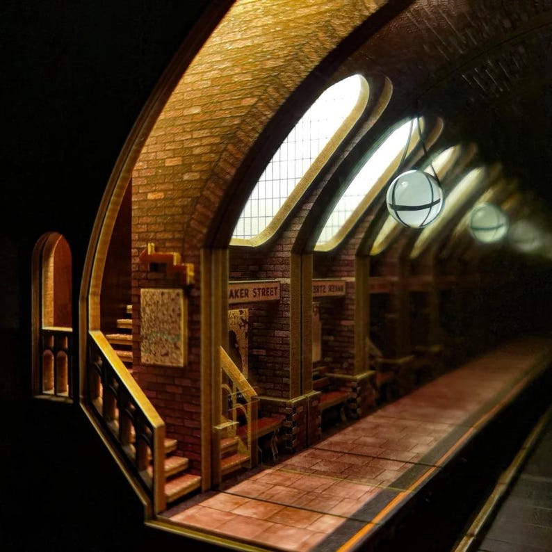 May include: A detailed miniature model of a vintage subway station. The scene features brick walls, arched ceilings, and the words "Baker Street" on a sign. The platform has benches and is illuminated by hanging globe lights.