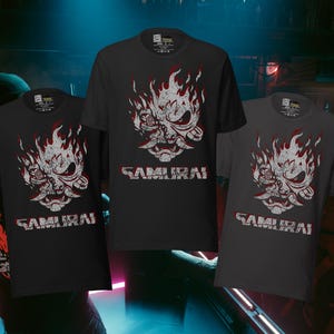 May include: Three black and gray t-shirts with a graphic of a flaming samurai mask and the word "SAMURAI" in white. The shirts are short-sleeved and have a crew neck.