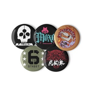 Könnte beinhalten: Eine Sammlung von fünf runden Buttons mit verschiedenen Designs. Ein Button zeigt einen weißen Totenkopf mit dem Wort "MAELSTROM" darunter. Andere Buttons zeigen Text und Grafiken, darunter einen Tiger und eine Schlange.