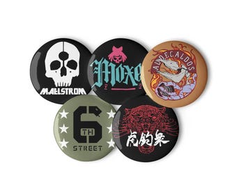 May include: A collection of five round buttons with various designs. One button features a white skull with the word "MAELSTROM" below. Other buttons display text and graphics, including a tiger and a snake.