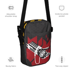 Puede incluir: Bolso bandolera negro con un diseño gráfico rojo y blanco. Cuenta con una correa ajustable para el hombro, cremallera de dos vías y bolsillos interiores y exteriores. La bolsa está hecha de tela resistente.