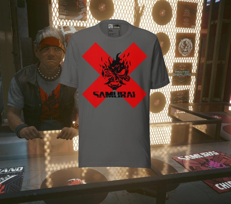 May include: Gray t-shirt featuring a red cross design with a black samurai graphic and the word "SAMURAI" in black. The shirt is displayed in a shop setting with vinyl records and a person in the background.