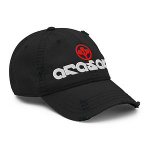 May include: Black distressed baseball cap with the white word "arasak" and a red emblem. The cap has a curved brim and a distressed, worn look, with frayed edges.