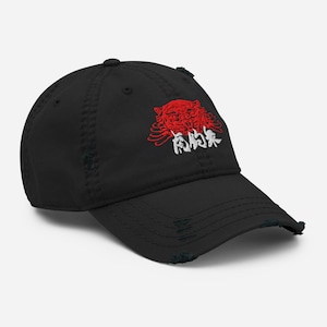 May include: Black distressed baseball cap with a red and white embroidered design. The design features a red tiger head and white Japanese characters. The cap has a curved peak and a worn, vintage appearance.