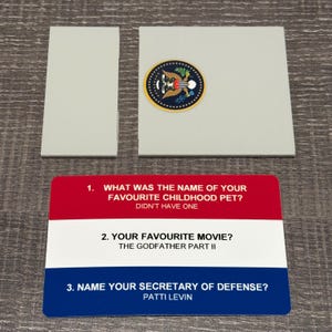 May include: A game card with red, white, and blue stripes, featuring three questions and answers. The questions are about a favorite childhood pet, movie, and Secretary of Defense. Two gray rectangular pieces are also present.