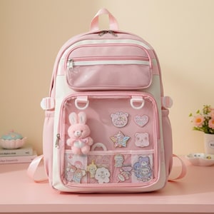 Könnte beinhalten: Rosa-weißer Rucksack mit einer transparenten Vordertasche, in der sich ein Plüschhase und verschiedene dekorative Aufkleber befinden. Der Rucksack hat mehrere Fächer, einen oberen Griff und verstellbare Träger.