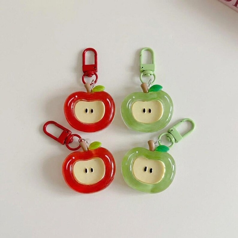 May include: Four apple-shaped keychains, two red and two green, with a white center and a small green leaf. Each keychain has a metal clasp for attaching to keys or bags. The keychains are a fun accessory.