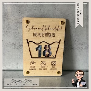 Op de afbeelding: Een houten bord met de tekst "Schonend behandela! DAS GUTE STÜCK IST 18" en wassymbolen. Het bord wordt bij elkaar gehouden door vier goudkleurige schroeven. De onderkant van het bord heeft de tekst "Digitale Datei".