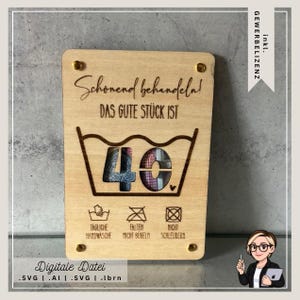 Op de afbeelding: Houten plaat met gegraveerde tekst en een wassymbool met het nummer 40 erin. De plaat bevat ook wasinstructies en de tekst "Schonend behandeln! DAS GUTE STÜCK IST".