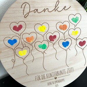 Puede incluir: Una placa redonda de madera con la palabra "Danke" en cursiva. Presenta globos en forma de coraz&oacute;n en varios colores, incluyendo rojo, amarillo y azul. Tambi&eacute;n est&aacute; presente el texto "F&Uuml;R DIE KUNTERBUNTE ZEIT!" y "DEINE BLUMENGRUPPE 2025".