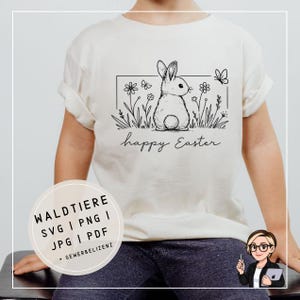 Op de afbeelding: Crèmekleurig T-shirt met een zwart-witte illustratie van een konijn, bloemen en een vlinder in een rechthoekig kader. De woorden "happy Easter" staan eronder. Onderaan is een cirkelvormige afbeelding met tekst zichtbaar.