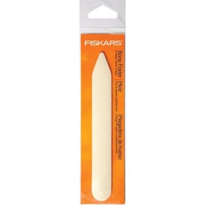 Puede incluir: Un plegador de hueso blanco en un paquete de plástico transparente con fondo naranja. El paquete tiene el texto "FISKARS" y "Bone Folder Plioir" impreso.