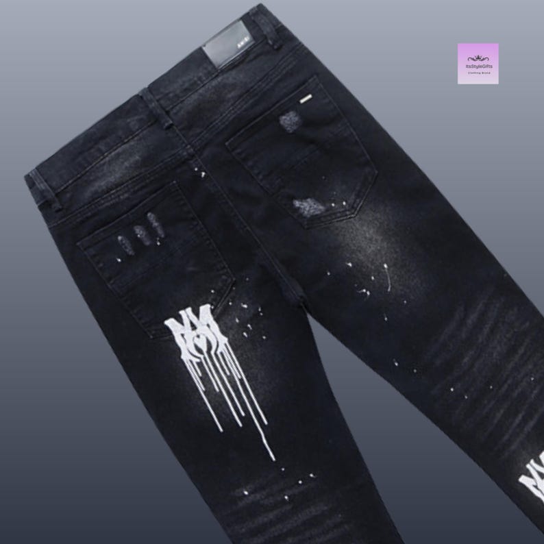 May include: Black denim jeans with distressed details and white paint splatter accents. The jeans feature a classic five-pocket design and a logo detail on the back pocket. A stylish and modern look.