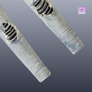 以下が含まれることがあります： ライトブルーのデニムジーンズ。ダメージ加工が施されており、破れた部分から黒い生地が見えています。画像はジーンズの脚の下部をクローズアップし、その質感とデザインを強調しています。