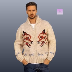 May include: Cream-coloured zip-up sweater with a fox design on the front. The sweater features a shawl collar, two front pockets, and blue and grey leaf patterns on the sleeves. The fox design is red, black, and white.