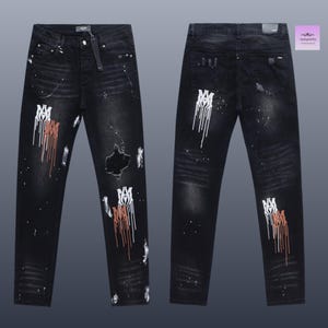May include: Black denim jeans with distressed details, featuring white and brown paint splatter and a ripped knee. The jeans have a straight leg cut and a button and zipper closure. The front and back of the jeans are visible.