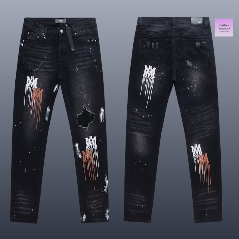 May include: Black denim jeans with distressed details, featuring white and brown paint splatter and a ripped knee. The jeans have a straight leg cut and a button and zipper closure. The front and back of the jeans are visible.