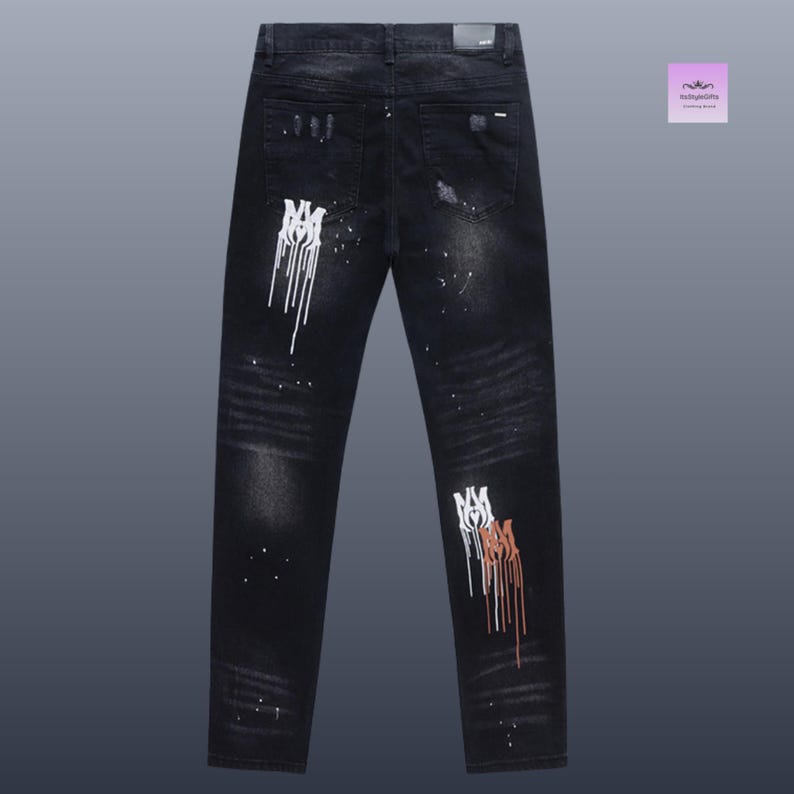 May include: Black denim jeans with distressed details and white and brown paint splatter accents. The jeans feature a unique design with a logo on the legs. A stylish and edgy fashion item.