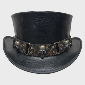 May include: A black top hat with a textured finish featuring a wide band around the base. The band has a snakeskin-like pattern in shades of brown and gray, accented with silver-toned metal skull ornaments and small circular studs throughout.