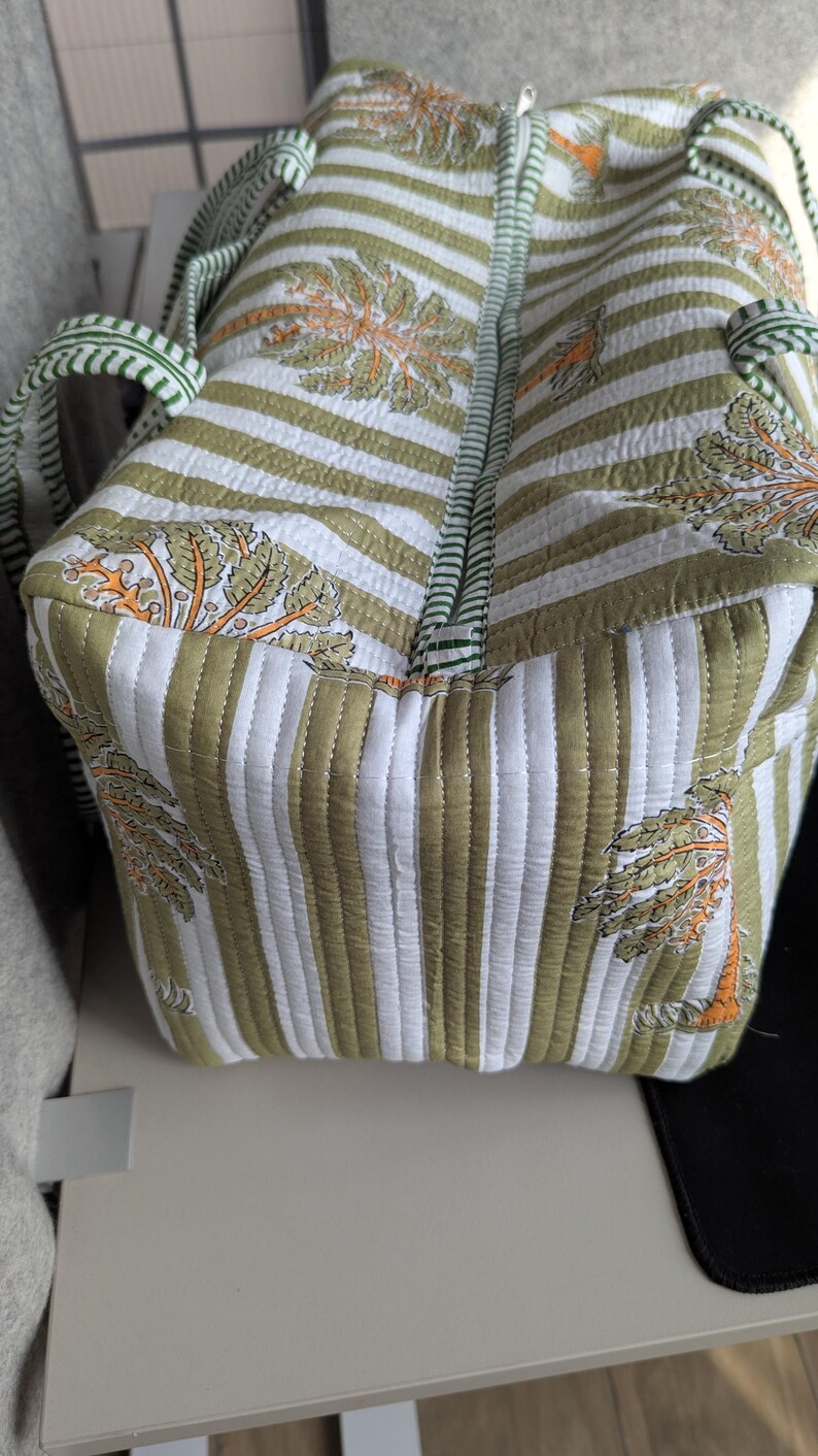 May include: Quilted tote bag with a striped pattern in white and olive green. The bag features a repeating design of stylized trees in orange and green. The handles and zipper trim are green.