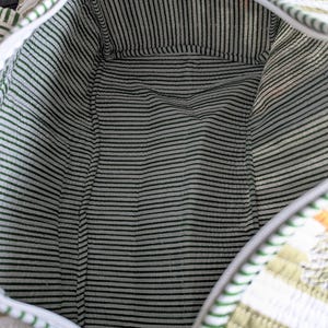 May include: Open view of a quilted travel bag with a green and white striped interior. The exterior features a green and white striped pattern with a palm tree design. The bag has a zipper closure and a white trim.