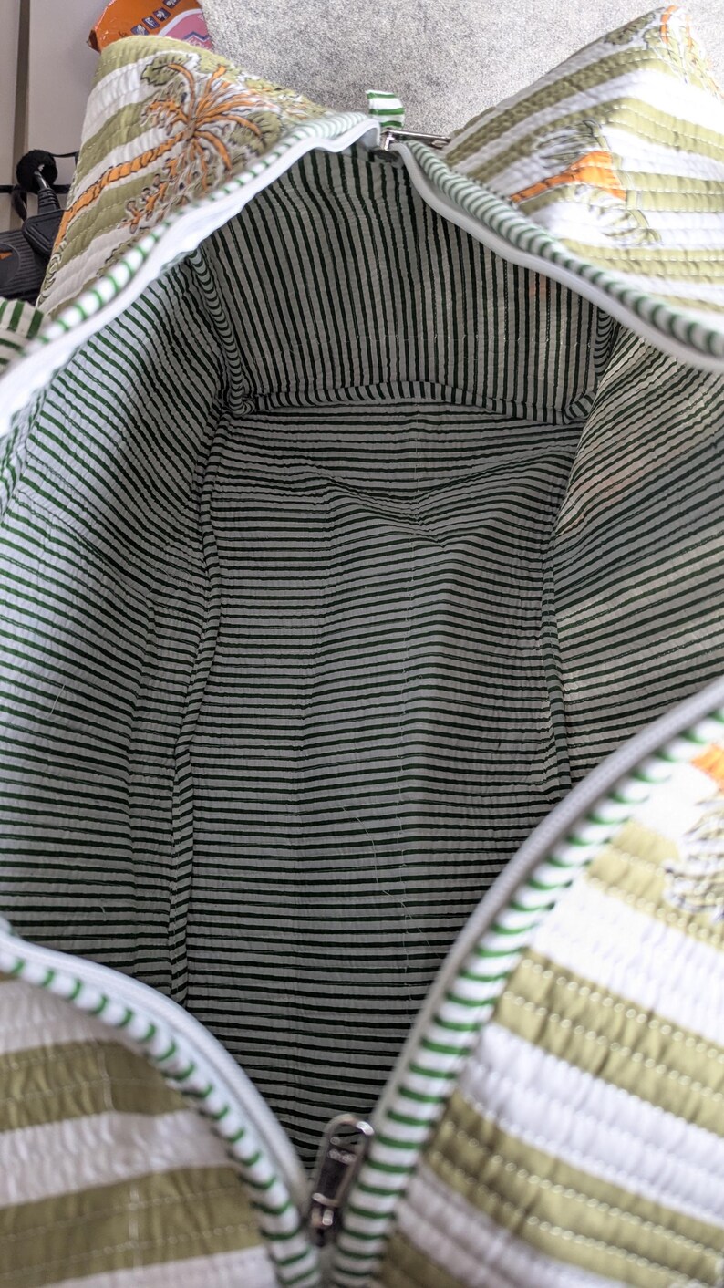May include: Open view of a quilted travel bag with a green and white striped interior. The exterior features a green and white striped pattern with a palm tree design. The bag has a zipper closure and a white trim.