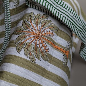 May include: Quilted fabric with a palm tree design. The fabric features a white and olive green striped pattern with a green striped border. The palm tree is orange and olive green.