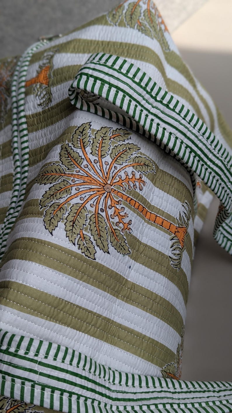 May include: Quilted fabric with a palm tree design. The fabric features a white and olive green striped pattern with a green striped border. The palm tree is orange and olive green.