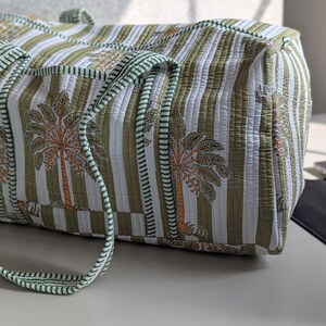May include: A quilted tote bag with a green and white striped pattern and palm tree motifs. The bag has green handles and trim. The bag is rectangular and appears to be made of a soft fabric.