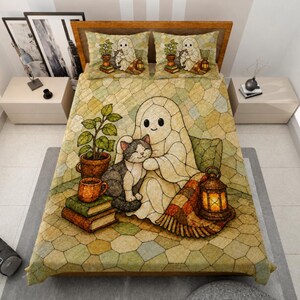 May include: A quilt and two pillowcases featuring a stained-glass style illustration of a ghost hugging a gray and white cat. The scene includes a potted plant, a stack of books, a mug, and a glowing lantern, all set against a beige mosaic background.