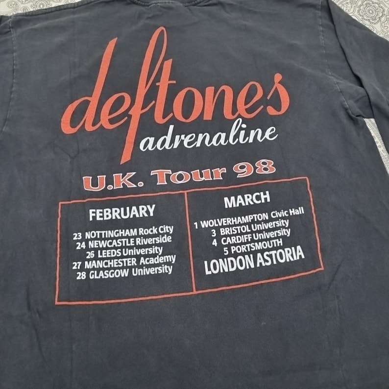 May include: Dark gray long-sleeve shirt featuring the band name "Deftones" in red script above the word "adrenaline". The shirt lists the U.K. Tour 98 dates and venues in red and white text.