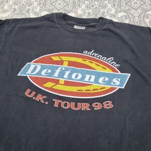May include: Dark gray t-shirt featuring the band name "Deftones" in a blue and white oval design with the word "adrenaline" above. The text "U.K. TOUR 98" is printed below in red. A vintage band tee.