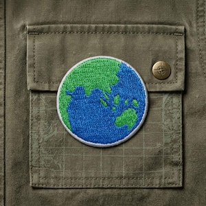 May include: Close-up of a green and blue embroidered Earth patch on a green jacket pocket. The patch is round with a white border. A gold-colored button with a compass design is visible.