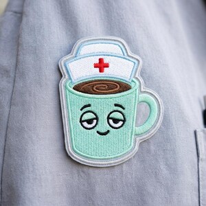 May include: Embroidered patch featuring a teal coffee mug with a sleepy face, topped with a nurse's cap and a red cross. The mug is filled with brown coffee. The patch is attached to a gray uniform.