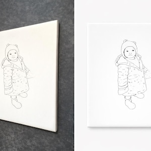 May include: A monochrome line drawing of a child in a hooded coat and boots, printed on a white canvas. The canvas is set against a dark grey background. The child's outfit includes a hat with bear ears.