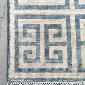 Könnte beinhalten: Nahaufnahme eines blau-cremefarbenen Teppichs mit einem geometrischen griechischen Schlüsselmuster. Der Teppich hat eine strukturierte Oberfläche und einen Fransenbesatz am unteren Rand. Der Teppich besteht aus einem weichen Material.