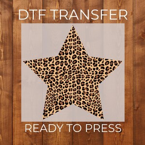 May include: A DTF transfer featuring a five-pointed star with a tan, brown, and black leopard print pattern. The text DTF TRANSFER is printed above the star, and the text READY TO PRESS is printed below the star in a clean white font.