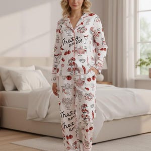 May include: White pajama set with a red trim and a repeating pattern of Italian food and drink illustrations. The words "That's amore" are printed on the top and pants. The long-sleeved top has a button-down front and a notched collar.
