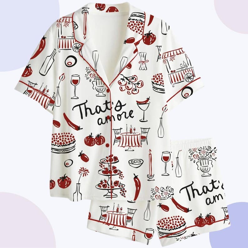 May include: White pajama set with a red trim and a repeating pattern of Italian food illustrations. The set includes a short-sleeved button-down shirt and matching shorts. The phrase "That's amore" is printed on the shirt and shorts.