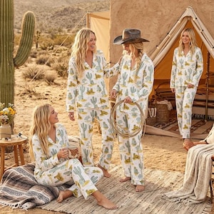 May include: Four people wearing matching white pajamas with a cactus and cowboy boot pattern. The group is gathered outdoors near a tent and a large cactus. One person is holding a lasso. The pajamas have a button-down shirt and pants.