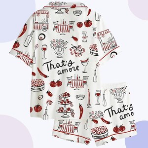 May include: White pajama set with a red trim and a repeating pattern of Italian food and drink illustrations. The set includes a short-sleeved top and shorts, with the phrase "That's amore" printed on both pieces.