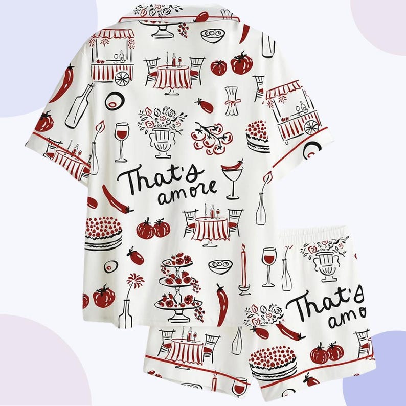 May include: White pajama set with a red trim and a repeating pattern of Italian food and drink illustrations. The set includes a short-sleeved top and shorts, with the phrase "That's amore" printed on both pieces.