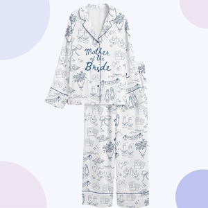 May include: White pyjama set with a blue floral and wedding-themed pattern. The top features the text "Mother of the Bride" in blue script. The set includes a button-down shirt with navy blue trim and matching trousers.